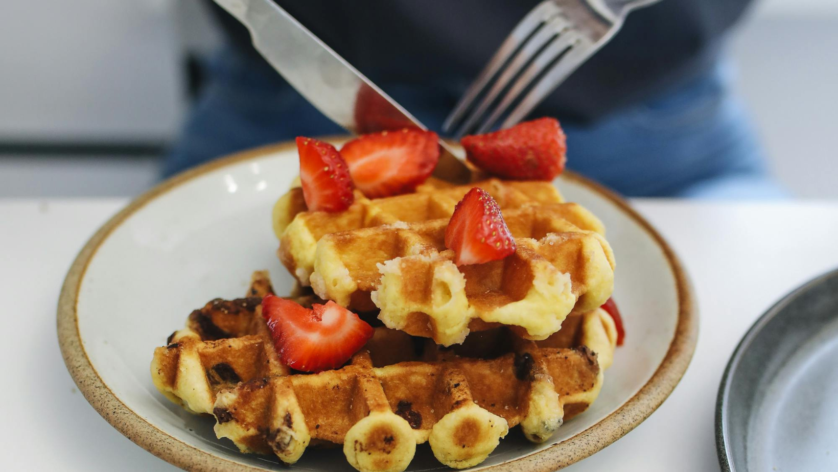 A plate of golden homemade strawberry waffles topped with fresh strawberries, whipped cream, and maple syrup, served on a rustic wooden table with a cozy kitchen setting.